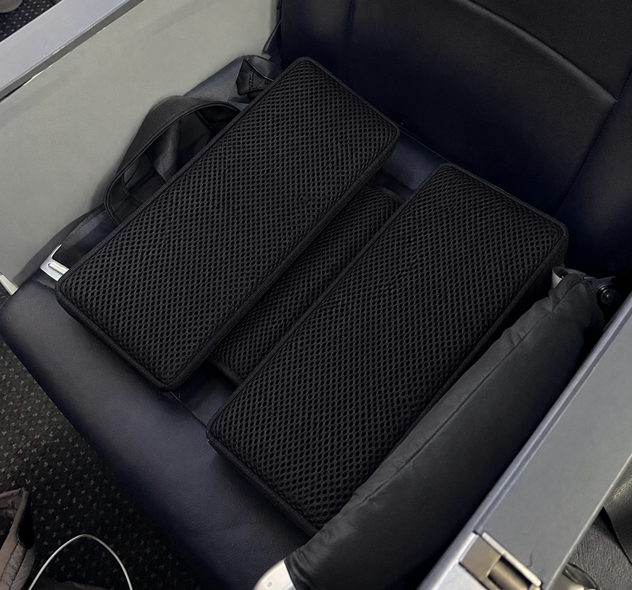 Black SunCloud® AirFlow travel seat cushion with full-surface cooling mesh shown on an airplane seat for cooler, more comfortable sitting.